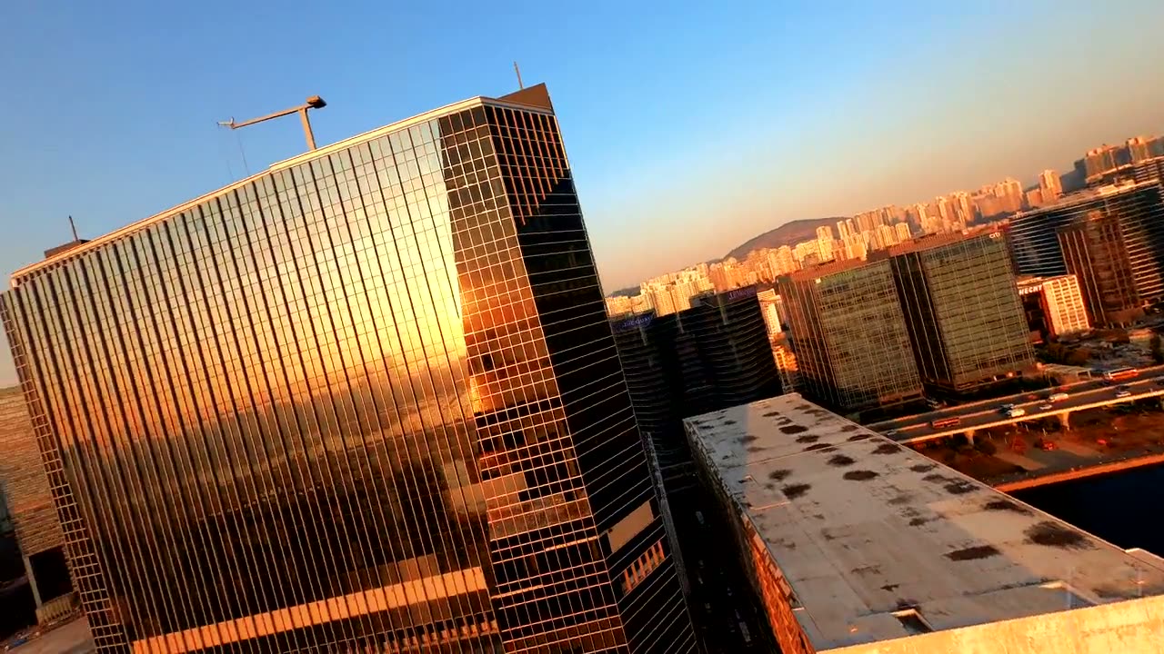 A drone rising alongside a bronze glass tower, the harbour and the city behind it.