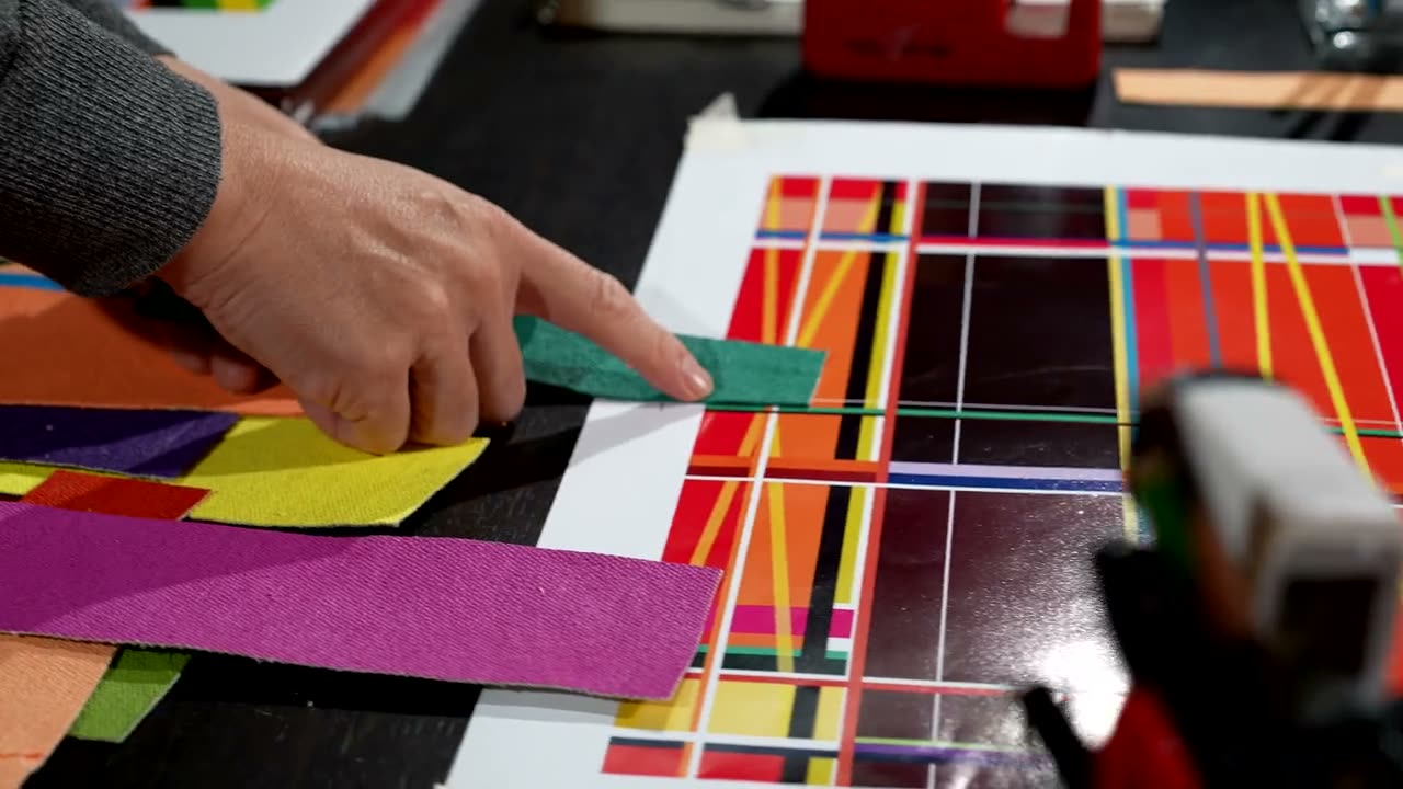Hands laying a line of coloured tape across a geometric composition on a board.