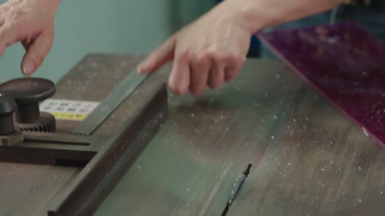 A worker handles a sheet of deep purple acetate on a cutting bench.