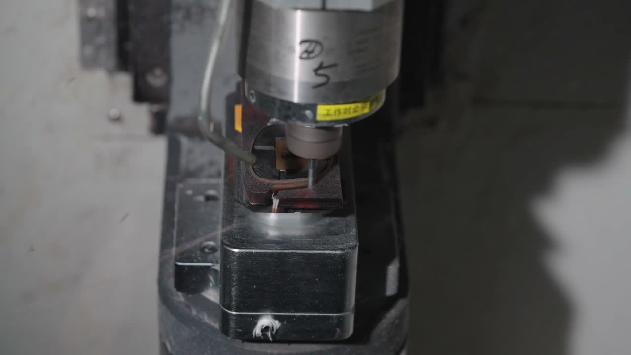 A CNC cutting head works on a clamped acetate blank.