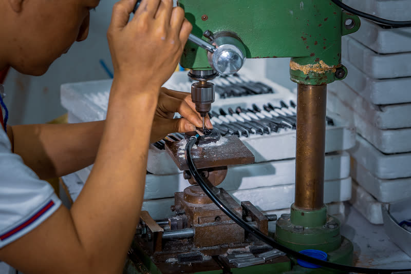 A technician at the drill press, a tray of tooling alongside.