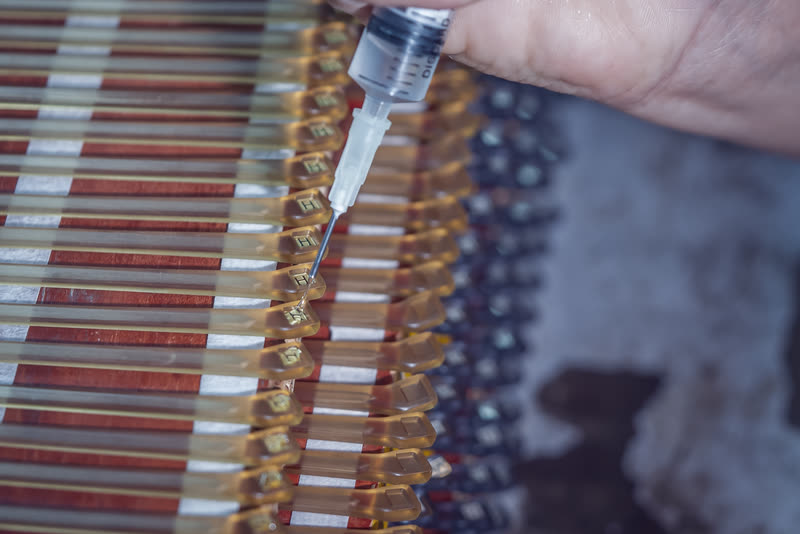 A hand runs epoxy along a rack of frames, one temple at a time.
