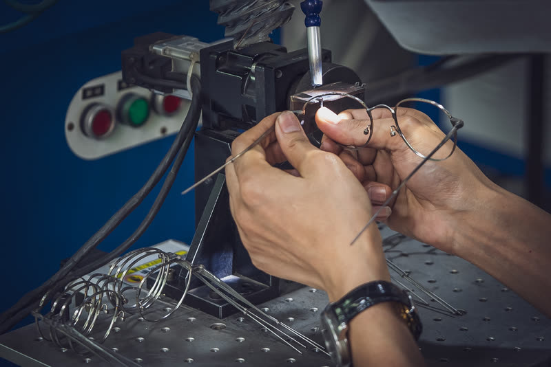 Two hands hold a wire front steady under the welding head.