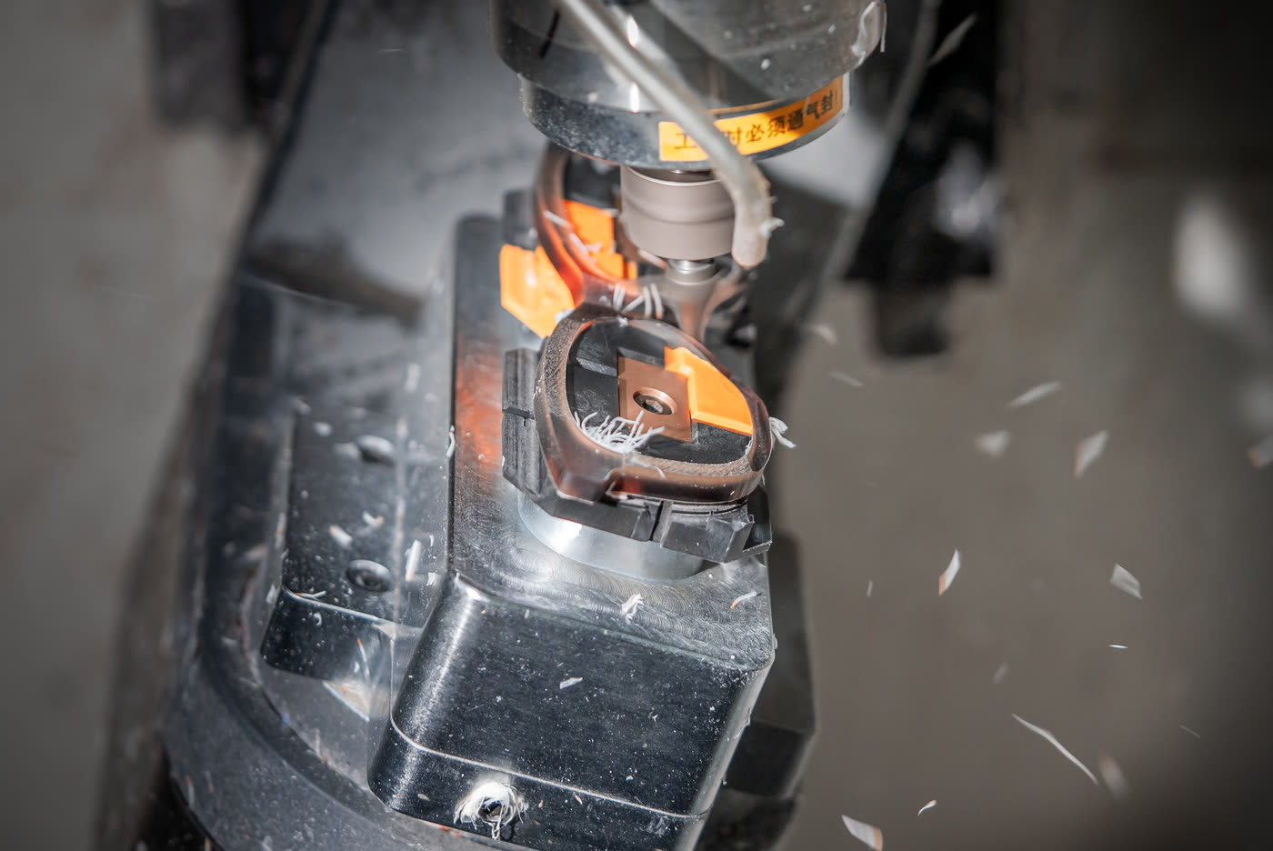 A cutter shaping an eyewear front clamped in an orange jig, swarf in the air around it.