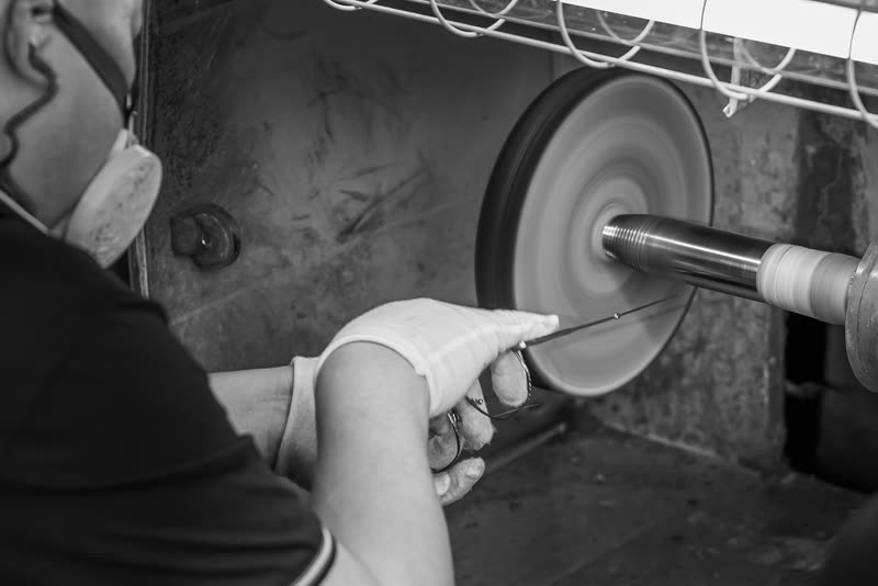 A gloved hand holds a frame against the polishing wheel.