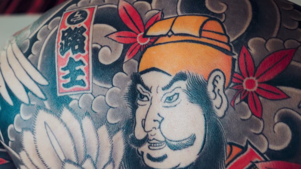 A close view of a tattooed face in Japanese style, under a red flower.