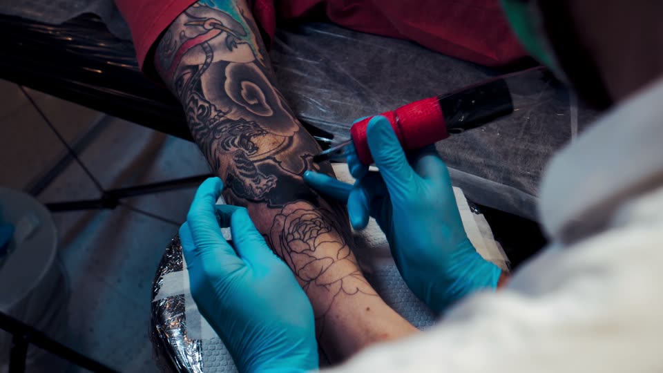 A gloved hand runs the machine along the outline of a peony on a forearm.