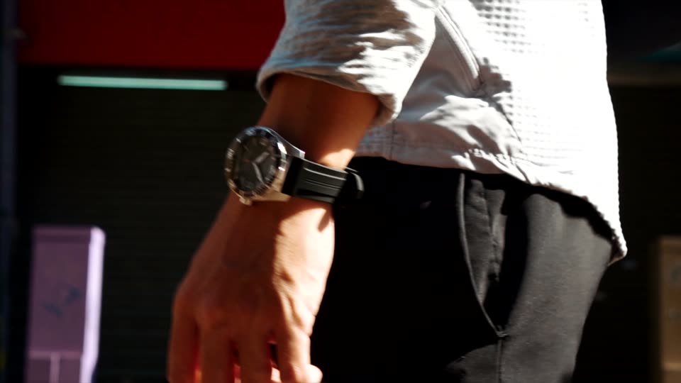 The watch on a black sports strap, worn with sportswear, mid-stride.